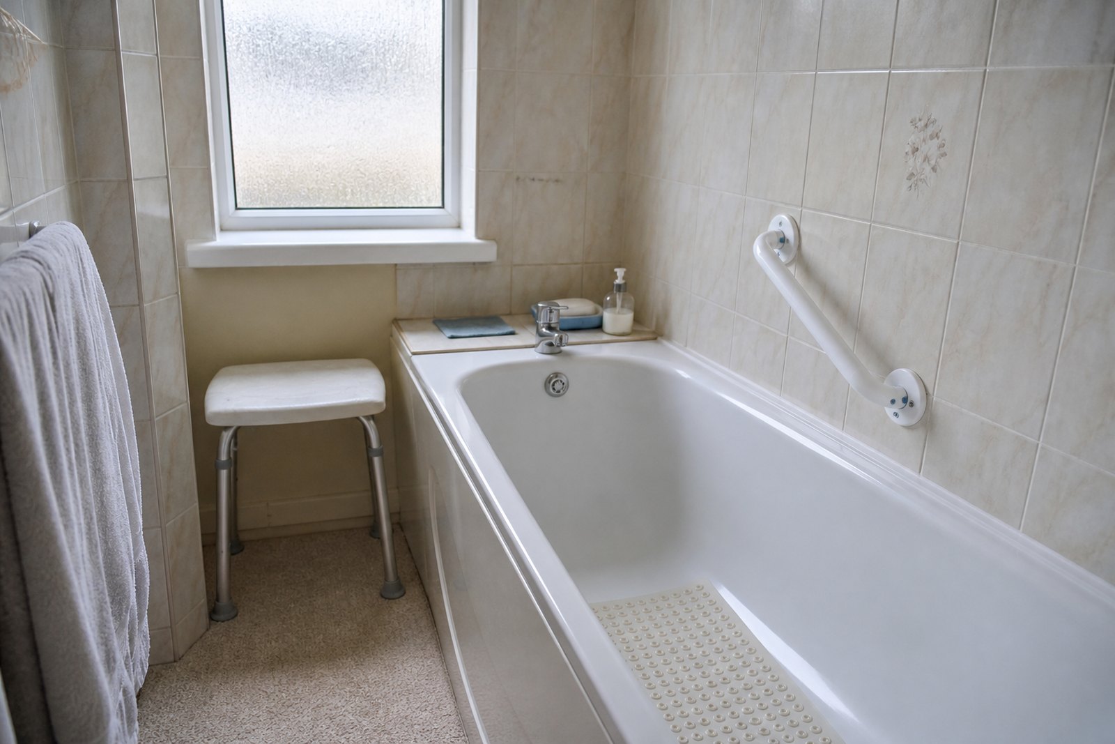 A domestic bathroom fitted with a grab rail, a non-slip bath mat and a shower stool