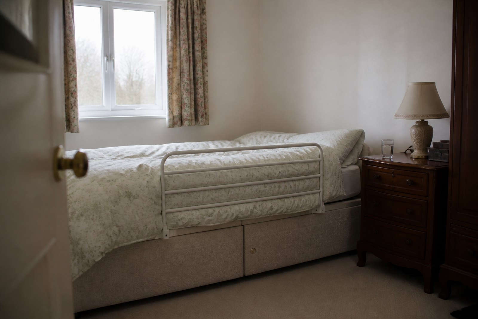A single bed in a domestic bedroom with a bed rail fitted along one side, close against the mattress