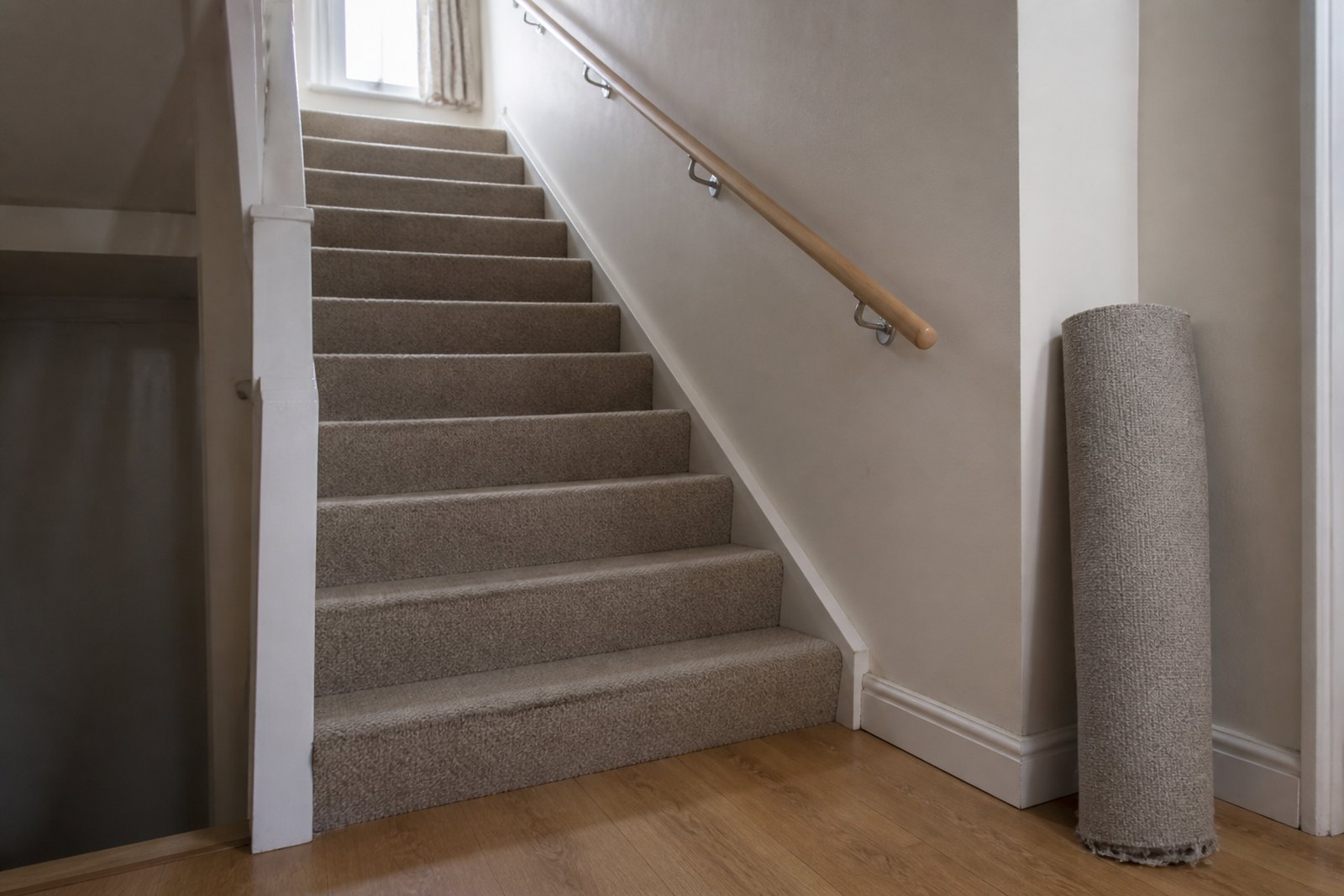 A well-lit carpeted staircase with a second handrail fitted and a loose rug rolled aside