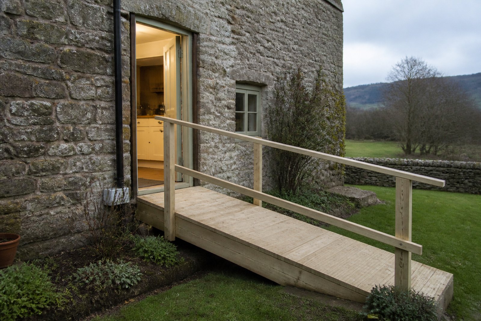 A widened cottage doorway with a gentle timber ramp and handrail into the garden