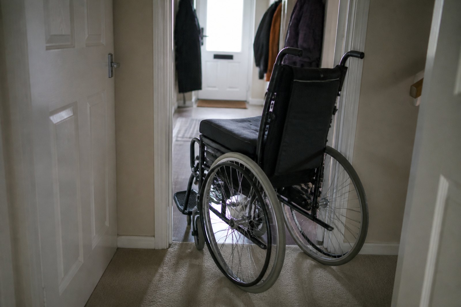 A self-propelled manual wheelchair in a home hallway, angled towards an open doorway