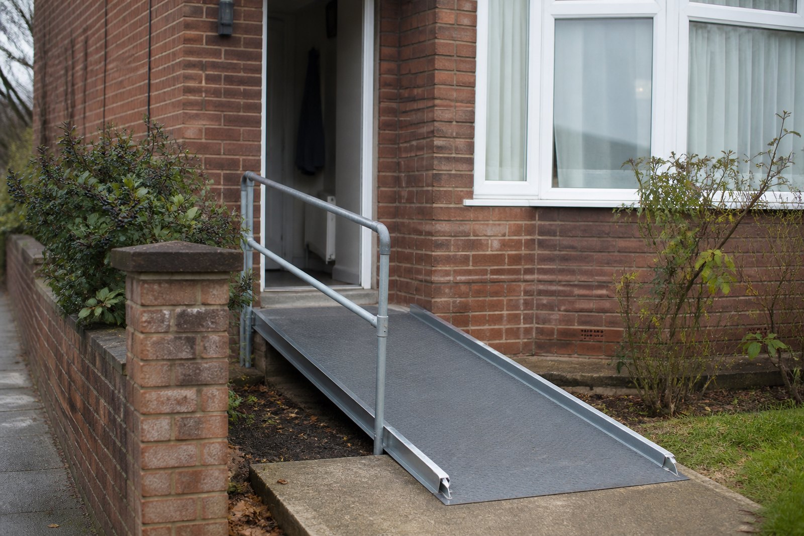 A gentle modular ramp with a handrail leading to the open front door of a semi-detached house