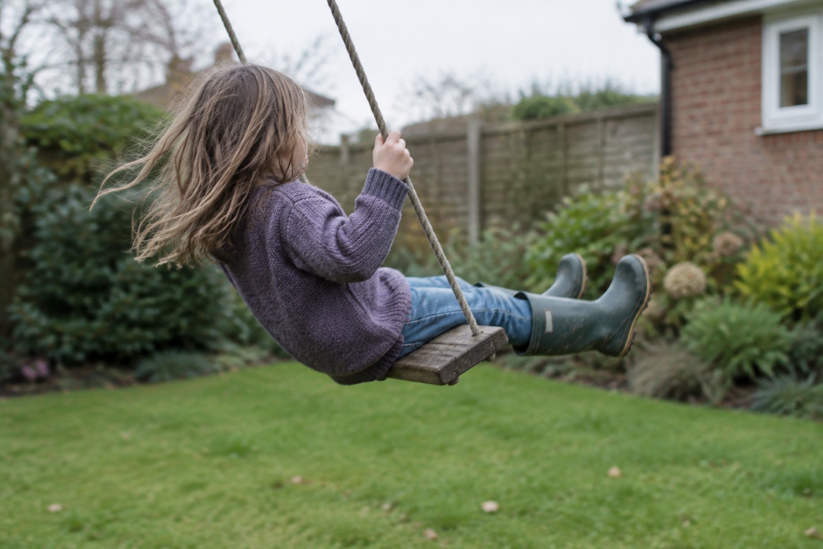 A child swinging on a garden swing, photographed from behind and to the side with the motion slightly blurred