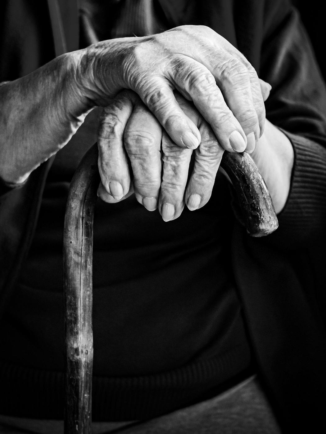 An older person's hands resting on a walking cane